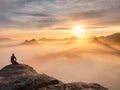 Tourist sit on peak of sandstone rock and watching into colorful mist and fog in morning valley. Sad man Royalty Free Stock Photo