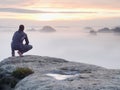 Tourist sit on peak of sandstone rock and watching into colorful mist and fog in morning valley. Sad man Royalty Free Stock Photo