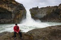 Tourist sits at the Aldeyjarfoss waterfall in northern Iceland