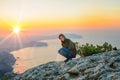 A tourist sits on a cliff overlooking the sea , watching the sun rise, travel concept