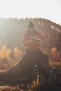 Tourist sitting on a fire pouring hot tea from a thermos into a cup at sunrise. A hiker is enlightened by the morning sun and