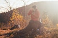 Tourist sitting on a stump eating porridge at sunrise. A hiker is enlightened by the morning sun and enjoys the view. Beskydy