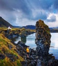 Tourist on a rocky beach looks at a small house in Arnarstapi, Iceland