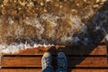 The tourist stands on a Wooden bridge. The transparent waves of the river and the rocky bottom. Shoes, top view Royalty Free Stock Photo