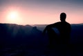 Tourist take a rest. Handsome young man sitting on the rock and enjoying view into misty rocky mountains. Royalty Free Stock Photo