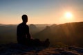 Tourist take a rest. Handsome young man sitting on the rock and enjoying view into misty rocky mountains. Royalty Free Stock Photo