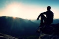 Tourist take a rest. Handsome young man sitting on the rock and enjoying view into misty rocky mountains. Royalty Free Stock Photo