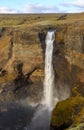 Tourist takes photo on mobile phone of second highest waterfall in Iceland - Haifoss. Picturesque sunrise view of deep canyon.