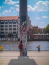 Tourist takes a photo of a sticker covered pole by a river in Berlin