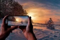 Tourist taking photo of sunset over winter landscape with covered in snow pine and fir trees against dramatic evening light. Snowy Royalty Free Stock Photo