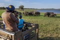A tourist taking photos of a herd of elephants grazing next to the tank at Minneriya National Park in Sri Lanka.