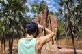 Tourist taking a picture of a big magnetic termite mound. Fit man holding camera, wearing casual clothes, cap and t-shirt.