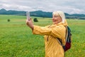 Tourist taking picture on her smartphone from top of mountain. Caucasian woman in hat and with backpack on rock. Travel Royalty Free Stock Photo