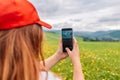 Tourist taking picture on her smartphone from top of mountain. Caucasian woman in hat and with backpack on rock. Travel Royalty Free Stock Photo