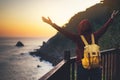 Tourist traveler with backpack standing with raised hands, hiker looking on sunset to valley in trip, hipster young girl enjoying Royalty Free Stock Photo