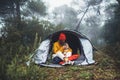 Tourist traveler in camp tent hugging red shiba inu on background froggy rain forest, hiker woman kiss puppy dog in mist nature Royalty Free Stock Photo