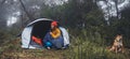 Tourist traveler hugging relaxation red shiba inu in camp tent on background froggy forest, hiker woman with puppy dog in mist Royalty Free Stock Photo