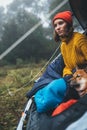 Tourist traveler relaxation red shiba inu in camp tent on background blue foggy forest, hiker woman with puppy in mist nature trip Royalty Free Stock Photo