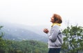 Tourist traveler standing on green top on mountain, young girl smiling and holding cup with hot drink against a background Royalty Free Stock Photo