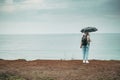 A tourist with an umbrella in the rain stands on a cliff and looks at the ocean from the back. tourist place.