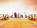 Tourist walk in autumn mist on wooden pier above sea. Rainy day Royalty Free Stock Photo