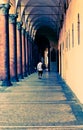 Tourist walking through a hallway with columns in Bologna Italy