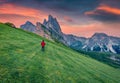 Tourist walks on green meadow at sunset with Furchetta peak on background.