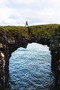 Tourist walks over a natural rock bridge in Arnarstapi, Iceland