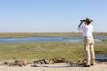 Tourist watching wildlife by binocular on Chobe River at sunrise. Chobe National Park, famous wildlilfe reserve and upscale travel Royalty Free Stock Photo