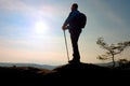 Tourist in windcheater with sporty trecking poles in hands stand on rocky view point.