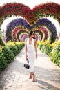 Young tourist woman walking in colorful heart shaped flowers alley in Dubai miracle garden in a sunny day