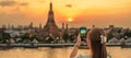 tourist woman enjoys view to Wat Arun Temple in sunset, Traveler take photo to Temple of Dawn by smartphone from rooftop bar. Royalty Free Stock Photo
