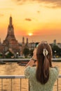 tourist woman enjoys view to Wat Arun Temple in sunset, Traveler take photo to Temple of Dawn by smartphone from rooftop bar. Royalty Free Stock Photo