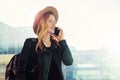 Tourist woman in hat with backpack is standing at airport and talking on cell phone. Girl stands, uses digital gadget. Royalty Free Stock Photo