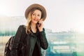 Tourist woman in hat with backpack is standing at airport and talking on cell phone. Girl stands, uses digital gadget. Royalty Free Stock Photo