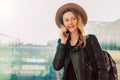 Tourist woman in hat with backpack is standing at airport and talking on cell phone. Girl stands, uses digital gadget. Royalty Free Stock Photo