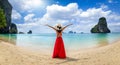 A tourist woman in a red dress stands at the beautiful Phra Nang beach at Krabi