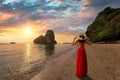 A tourist woman in a red dress stands at the beautiful Phra Nang Cave beach