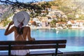 Tourist woman sits on a bench and enjoys the view to the idyllic village of Assos