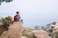 Tourist woman sitting with city backpack and enjoying ancient city harbor on the Ionian seacoast. Small Italian Castelmola Comune