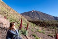 Tourist woman sitting in field of red flowers Tajinaste. Scenic view on volcano Pico del Teide, Mount El Teide National Park Royalty Free Stock Photo