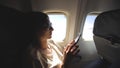 Tourist woman sitting near airplane window at sunset and using mobile phone during flight Royalty Free Stock Photo