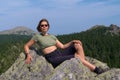 Woman with backpack relaxes on rock platform above valley Royalty Free Stock Photo