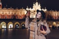 Tourist woman taking selfie on smartphone at night on Market square in Krakow Poland. Travel around Europe
