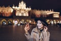 Tourist woman taking selfie on smartphone at night on Market square in Krakow Poland. Travel around Europe