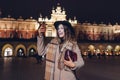 Tourist woman taking selfie on smartphone at night on Market square in Krakow Poland. Travel around Europe