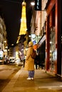 Woman in trench coat with backpack walking in night Paris