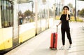 Tourist woman use smart phone with suitcase and wear total black. Traveller girl call taxi on train station Royalty Free Stock Photo