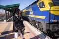 Tourist woman using phone on the station platform while a freight train is running. Royalty Free Stock Photo