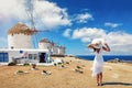 A tourist woman with white hat stands in front of the famous windmills at Mykonos, Greece